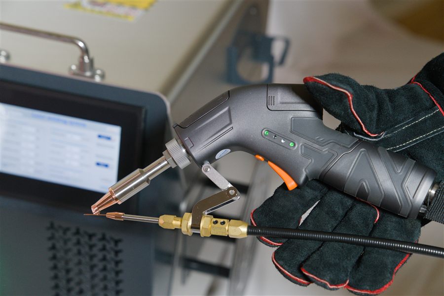 Gloved hand holding the handheld welding gun, showing grip-mounted controls and status LEDs