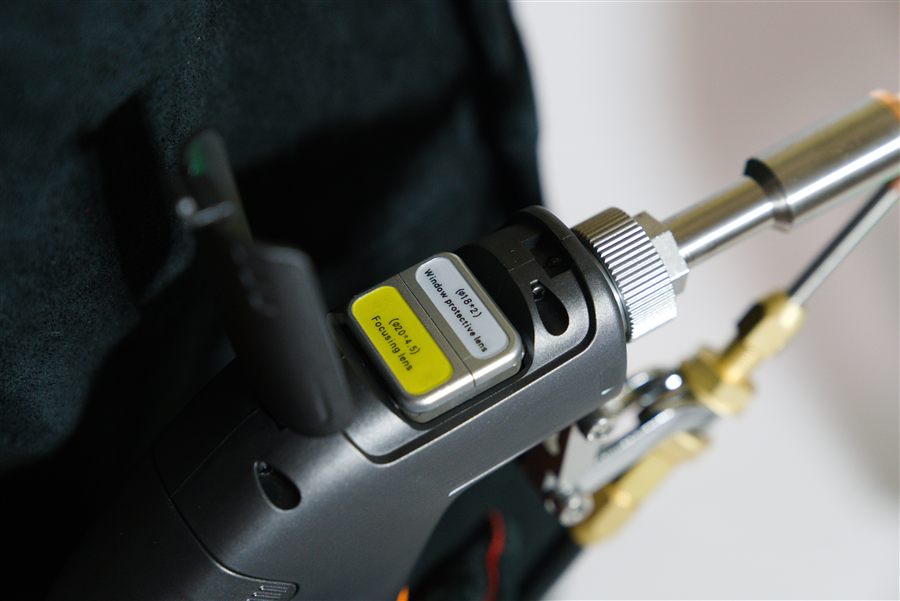 Close-up of the labeled focusing lens and window protective lens modules on the welding gun